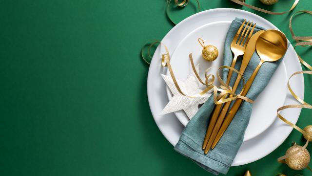 Christmas Flat Lay Background. Gold Cutlery with Bubbles served on napkin on plate on Green Background. Minimalistic design. Copy Space. Horizontal. Christmas concept. 