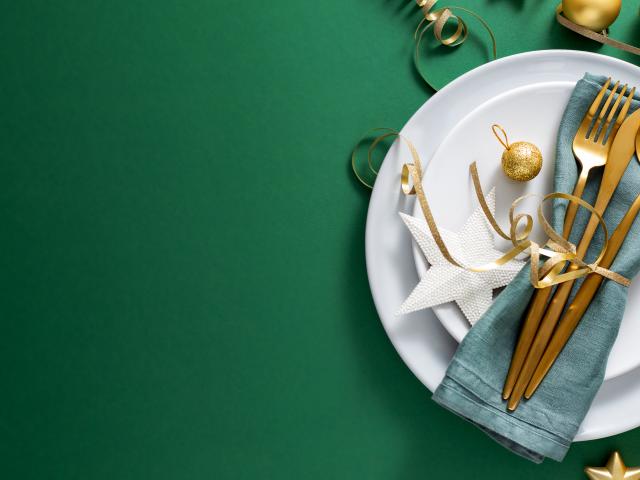 Christmas Flat Lay Background. Gold Cutlery with Bubbles served on napkin on plate on Green Background. Minimalistic design. Copy Space. Horizontal. Christmas concept. 