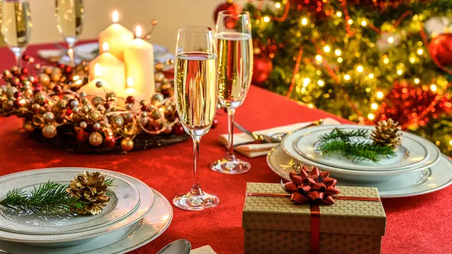 Beautifully decorated Christmas table - gift, glasses of champagne and tableware with Christmas decoration on a red tablecloth.