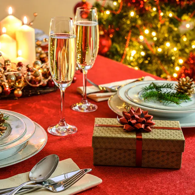 Beautifully decorated Christmas table - gift, glasses of champagne and tableware with Christmas decoration on a red tablecloth.