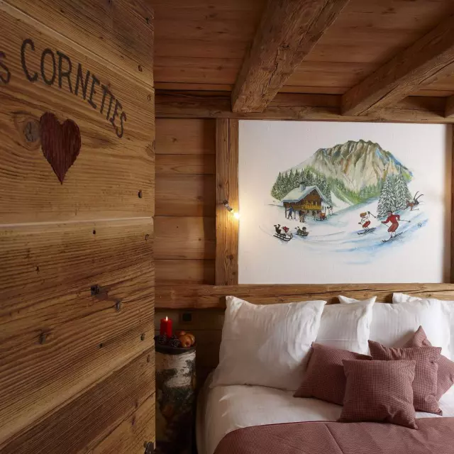 Chambre en bois, lit sur la droite avec un tableau de skieur au dessus