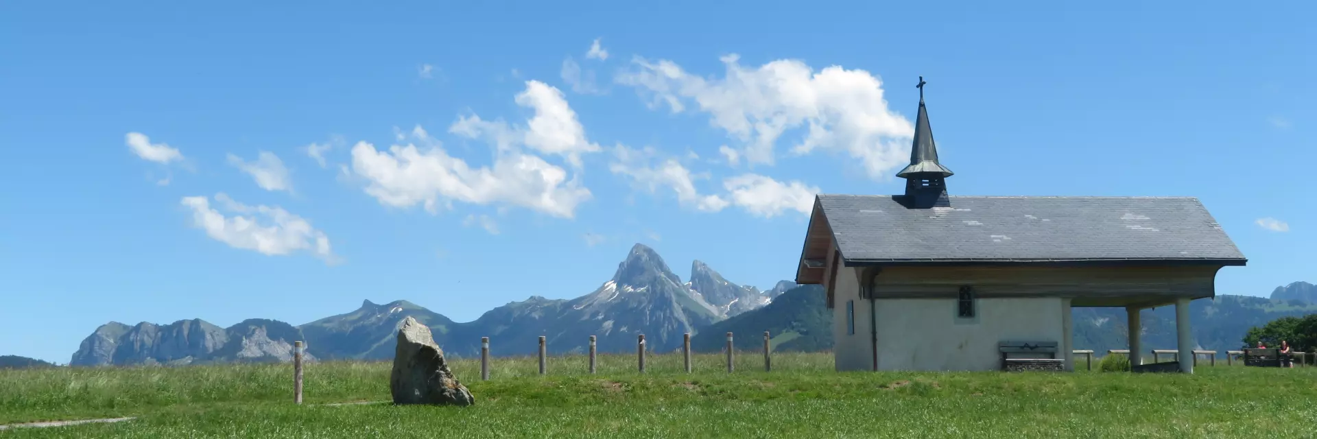 Chapelle de Champeillant against a blue sky and green grass. The Dent d'Oche peak stands out in the background.
