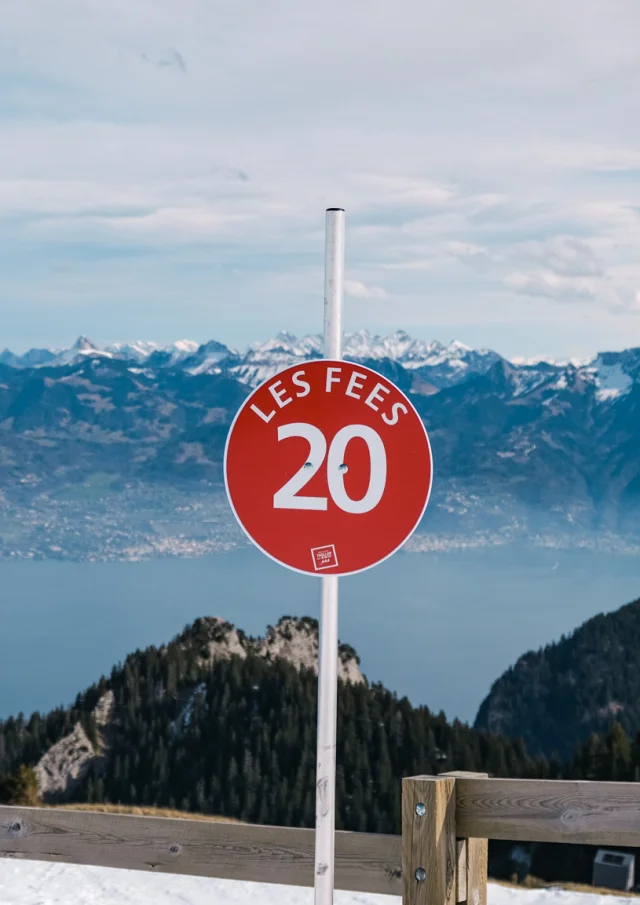 Haut Des Pistes De Ski Thollon Les Memises. In the foreground is a sign for the red Les Fées piste. In the background are Lake Geneva and the Swiss mountains.