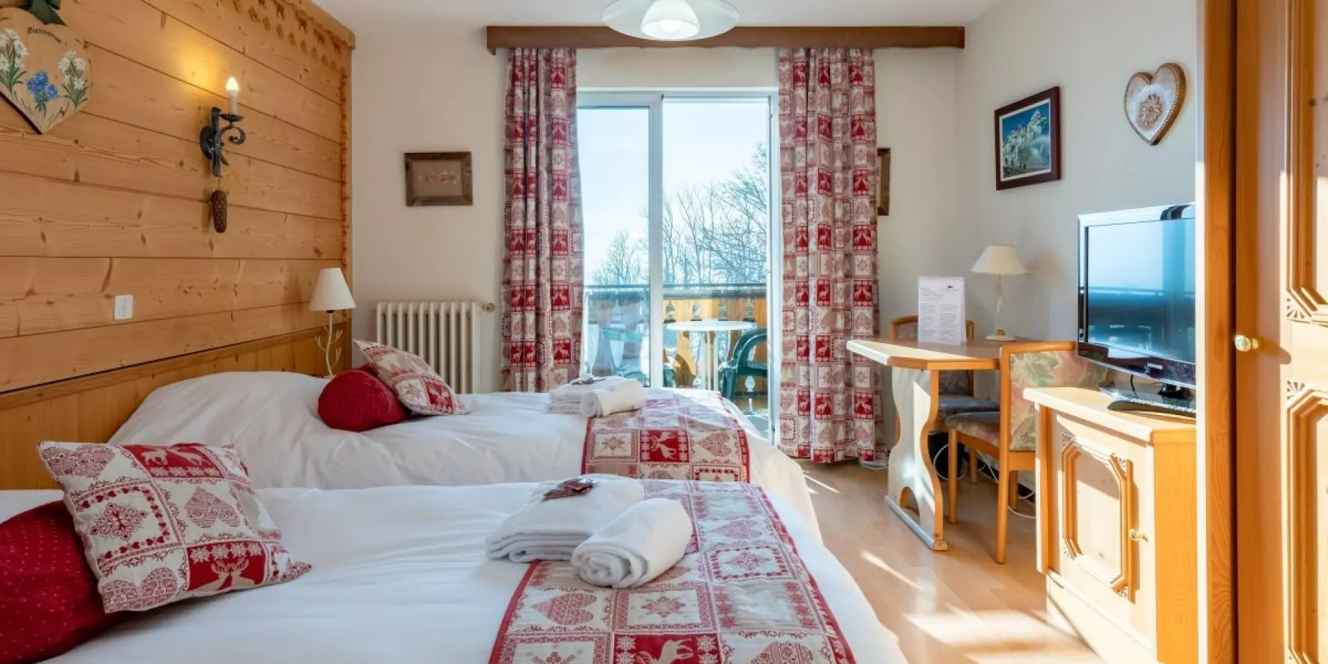 Hotel Le Bois Joli Saint Paul En Chablais. Chambre en bois lumineuse avec des lits blancs et des couvres lits rouges assortis aux rideaux.