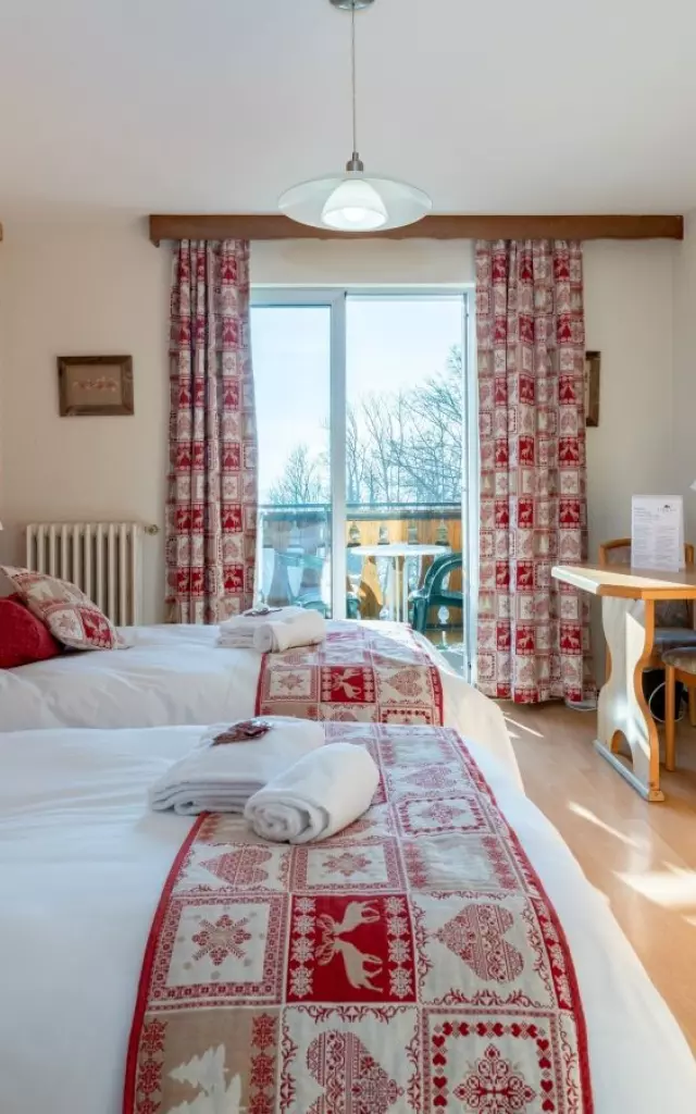 Hotel Le Bois Joli Saint Paul En Chablais. Chambre en bois lumineuse avec des lits blancs et des couvres lits rouges assortis aux rideaux.