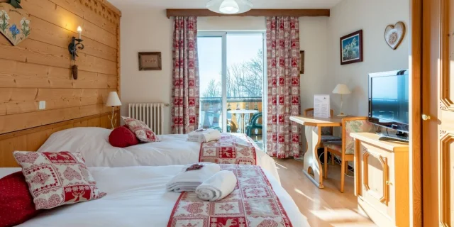 Hotel Le Bois Joli Saint Paul En Chablais. Chambre en bois lumineuse avec des lits blancs et des couvres lits rouges assortis aux rideaux.