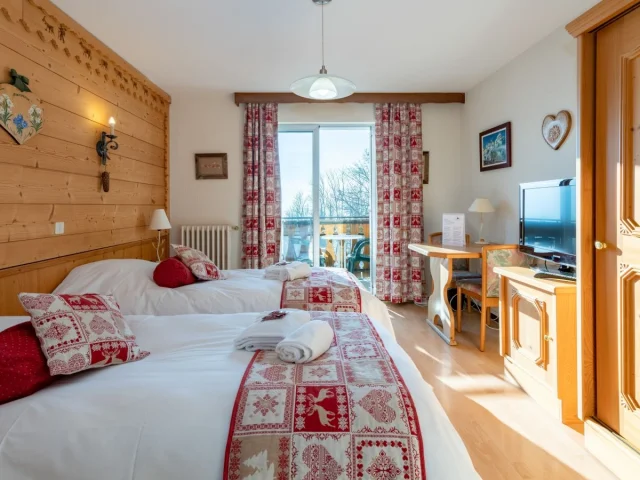 Hotel Le Bois Joli Saint Paul En Chablais. Chambre en bois lumineuse avec des lits blancs et des couvres lits rouges assortis aux rideaux.