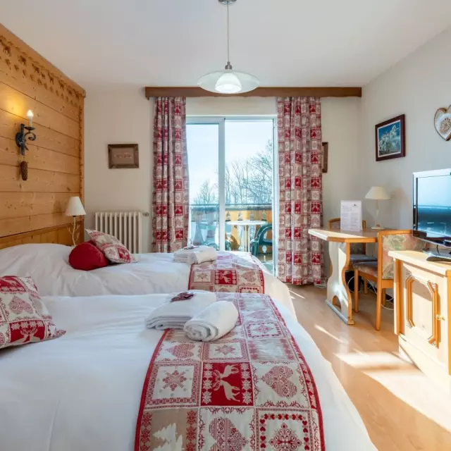 Hotel Le Bois Joli Saint Paul En Chablais. Chambre en bois lumineuse avec des lits blancs et des couvres lits rouges assortis aux rideaux.