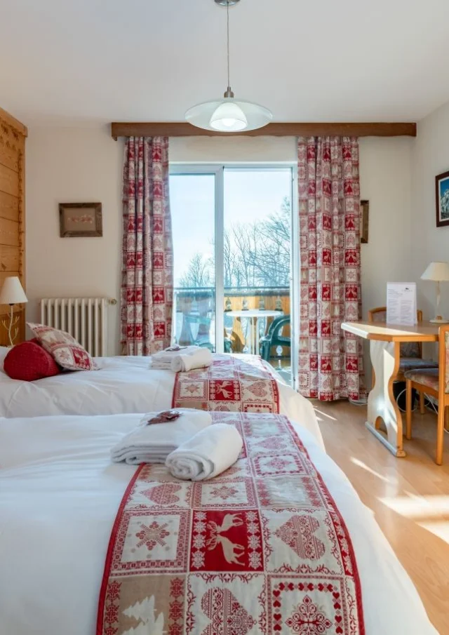 Hotel Le Bois Joli Saint Paul En Chablais. Chambre en bois lumineuse avec des lits blancs et des couvres lits rouges assortis aux rideaux.