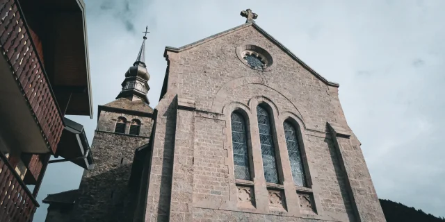 L’abbaye d’Abondance se situe au coeur des montagnes. La photo montre le parvis de l'Abbaye avec une immense façade en pierre grive et d'imposants vitraux sur le devant.