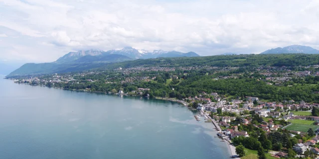 Lake and coast in the foreground. Buildings and trees can be seen from a drone view with the mountains in the background.