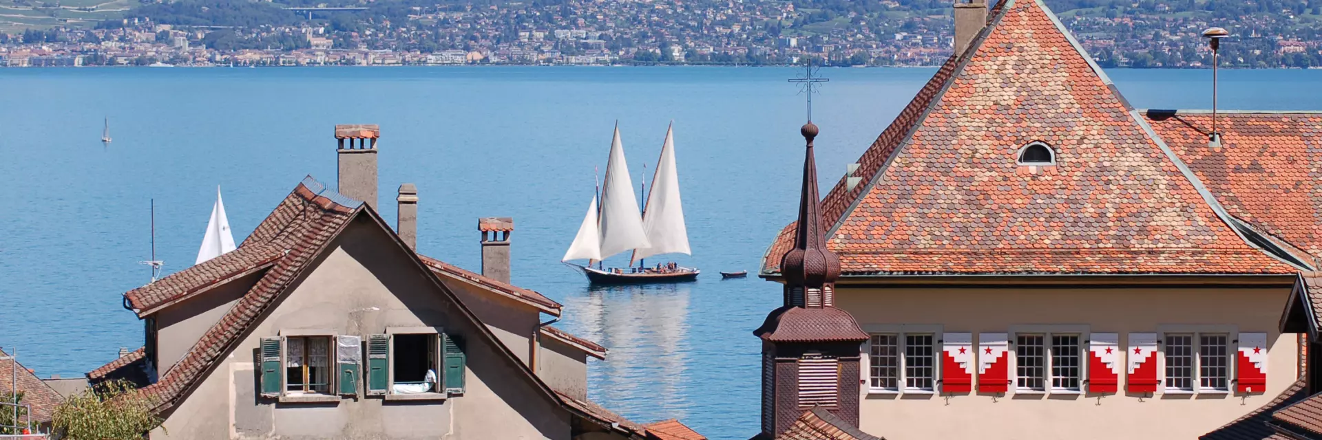 View of the lake, with a sailboat on the water and the buildings of St Gingolph in the foreground.