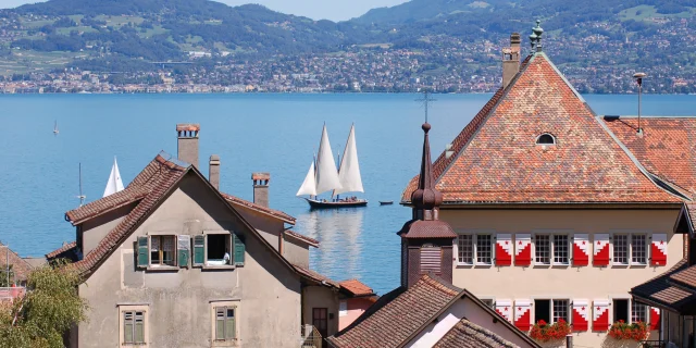 Vue sur le lac, on voit un voilier sur l'eau et les bâtiments de St Gingolph en premier plan