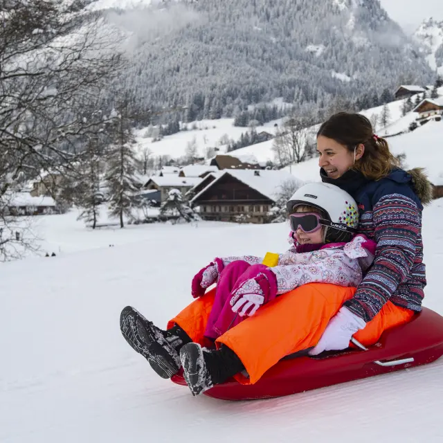 Un enfant et sa mère font de la luge en montagne, en hiver.