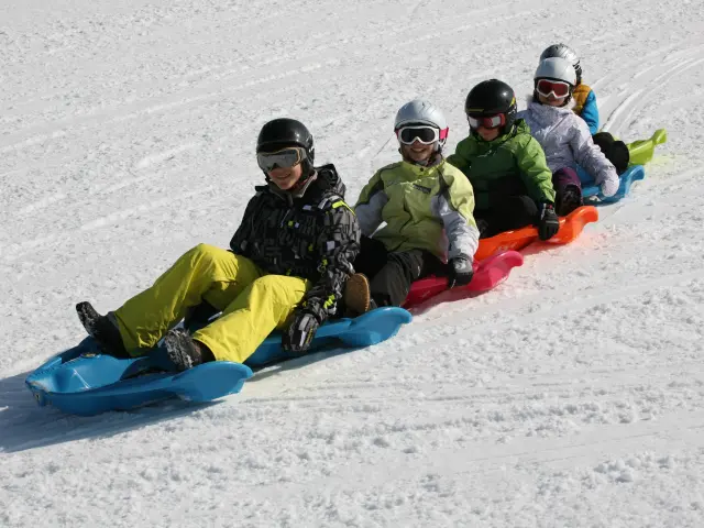 Des enfants et des adultes, souriants, en train de faire du snakegliss sur la neige, à Bernex