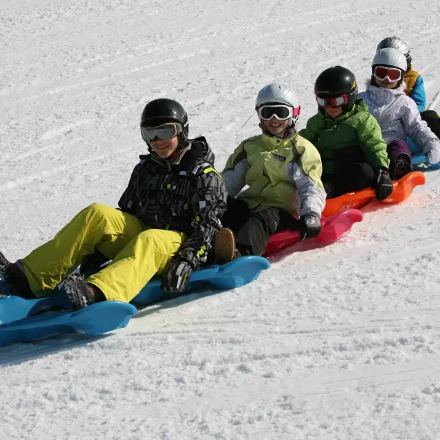 Des enfants et des adultes, souriants, en train de faire du snakegliss sur la neige, à Bernex