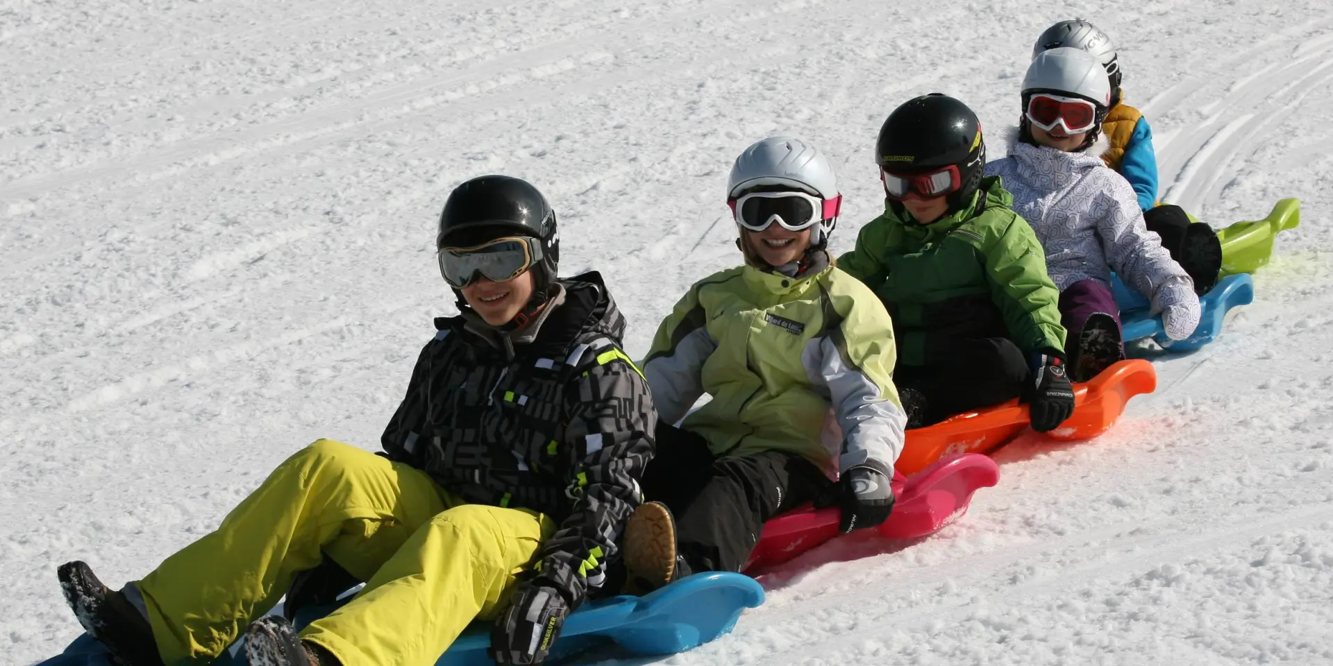 Des enfants et des adultes, souriants, en train de faire du snakegliss sur la neige, à Bernex