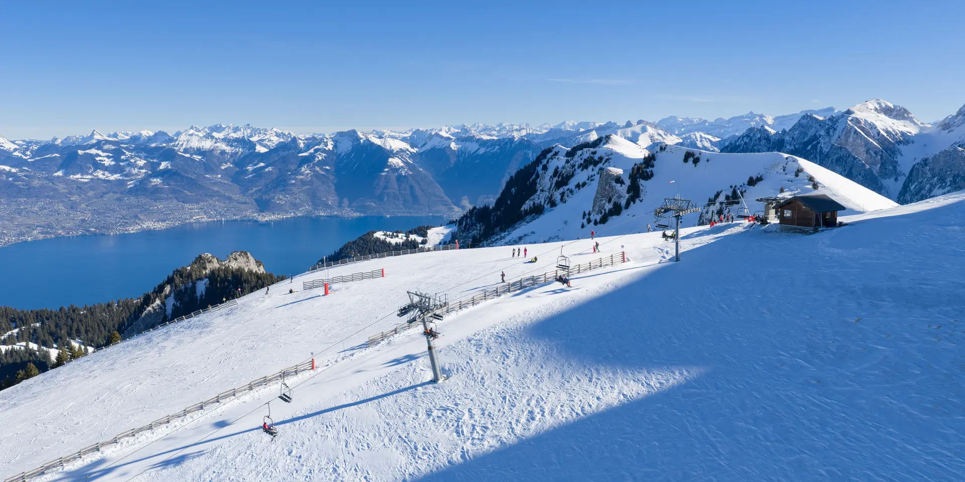 La station de ski de Thollon-les-Mémises, en plan large, enneigée, avec vue sur les montagnes suisses, le Léman, et sous un grand ciel bleu ainsi qu'un beau soleil éclatant