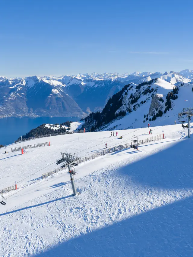 La station de ski de Thollon-les-Mémises, en plan large, enneigée, avec vue sur les montagnes suisses, le Léman, et sous un grand ciel bleu ainsi qu'un beau soleil éclatant