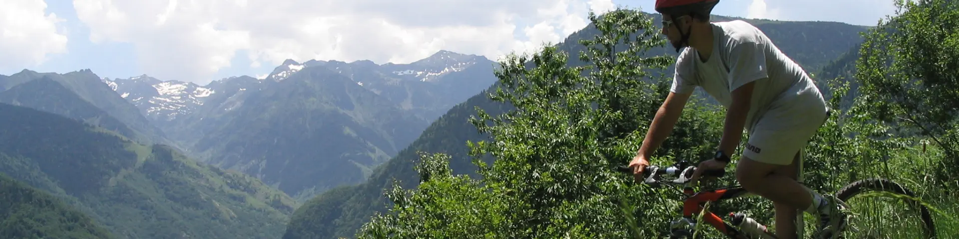 A cyclist in shorts and a red helmet pedaling on a mountain trail