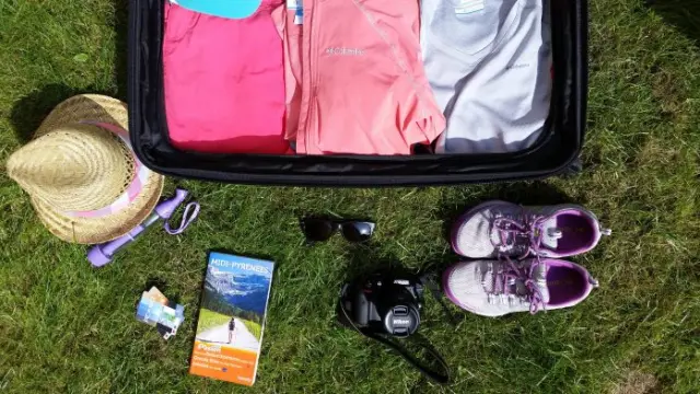 An open travel bag with clothes, shoes, a hat, sunglasses, and a camera