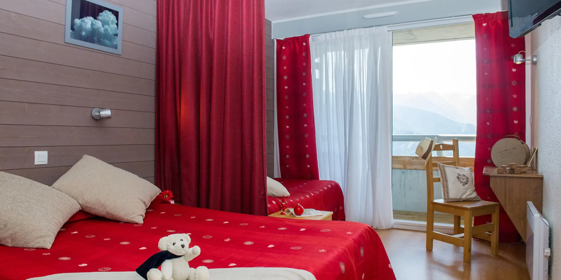 Chambre avec lit double rouge, rideaux rouges, vue sur la montagne