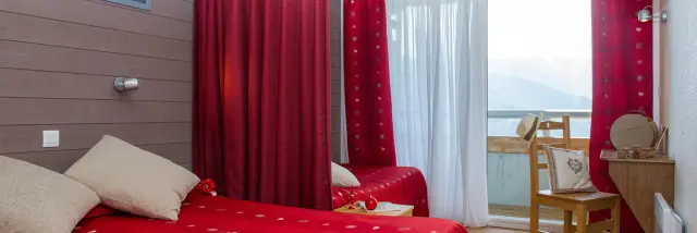 Bedroom with a double red bed, red curtains, mountain view