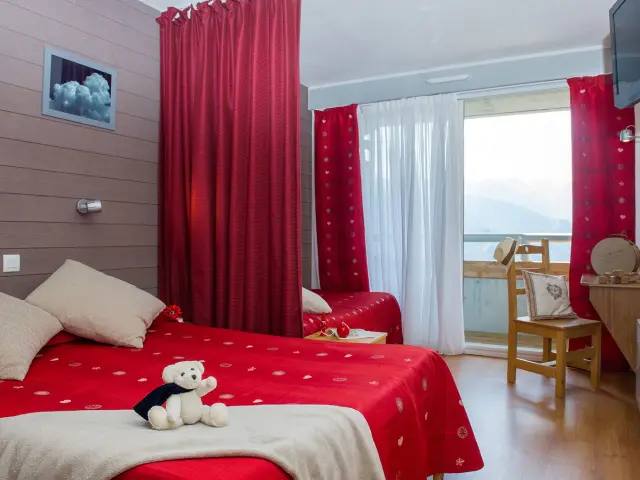 Chambre avec lit double rouge, rideaux rouges, vue sur la montagne