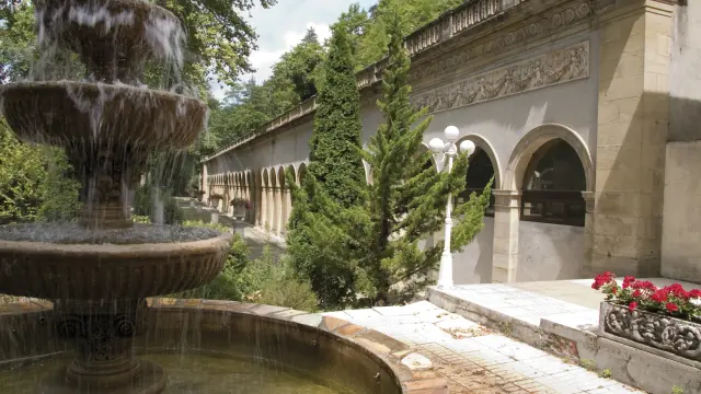 Fountain with multiple water levels in a garden surrounded by vegetation and an old building