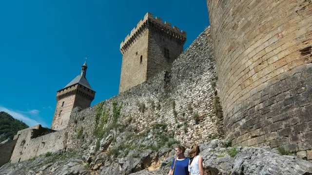 Two people in front of a medieval fortress with towers and stone walls