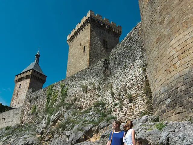 Deux personnes devant une forteresse médiévale avec des tours et des murs en pierre