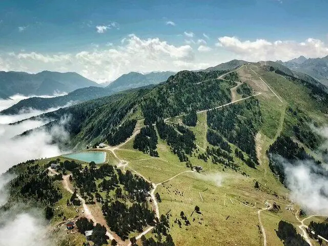 Vista aérea de montañas verdes con nubes bajas y un pequeño lago