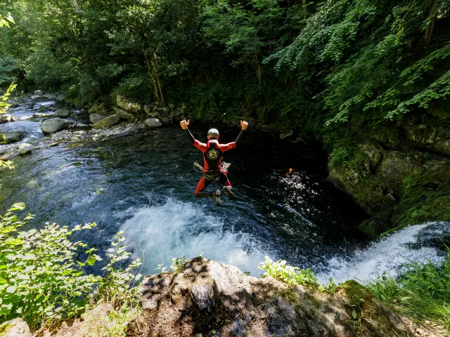 Une personne en combinaison rouge saute dans un canyon avec un fleuve en contrebas