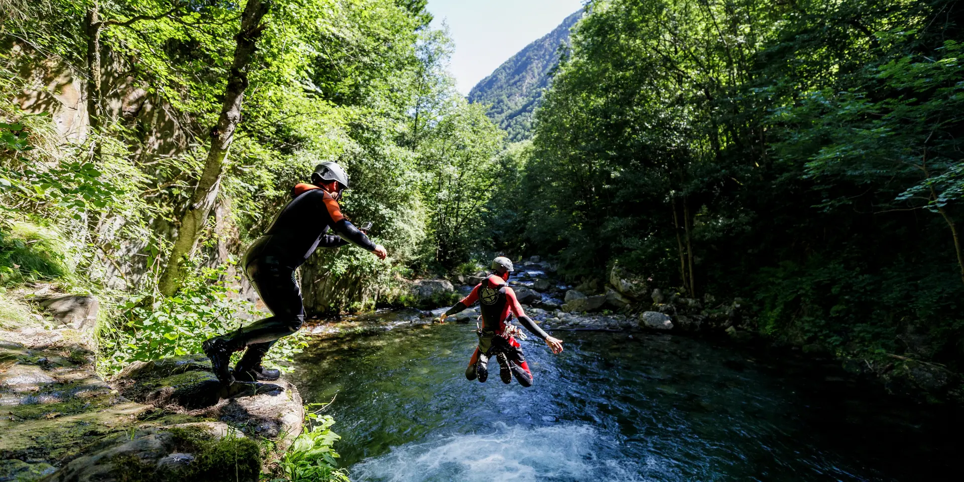 Deux personnes pratiquant le canyonisme dans un cours d'eau entouré de végétation