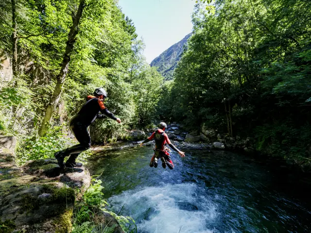 Deux personnes pratiquant le canyonisme dans un cours d'eau entouré de végétation