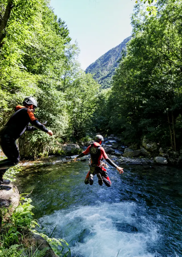 Deux personnes pratiquant le canyonisme dans un cours d'eau entouré de végétation