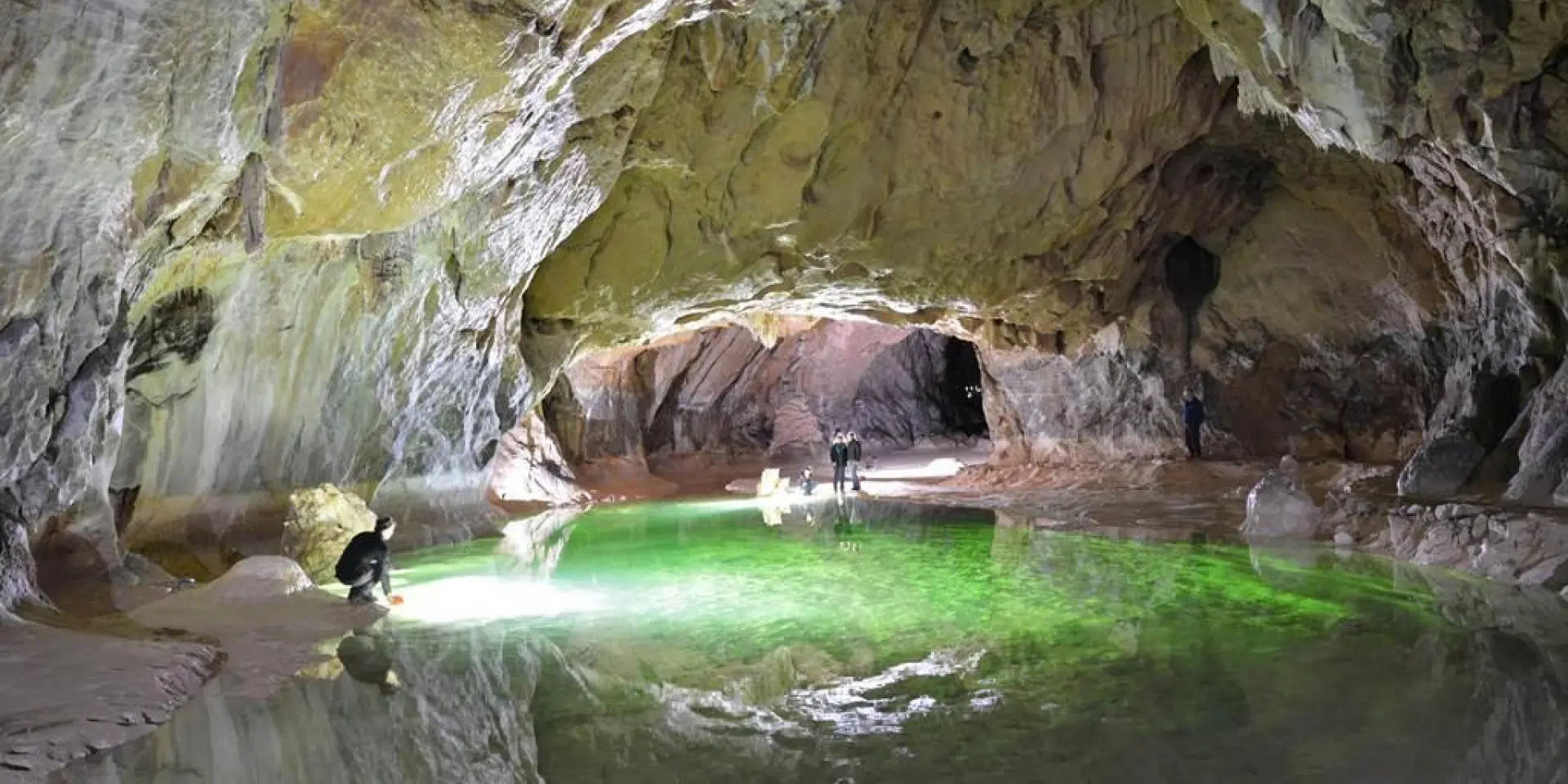 Explorers in a cave with a green light emanating from a pool