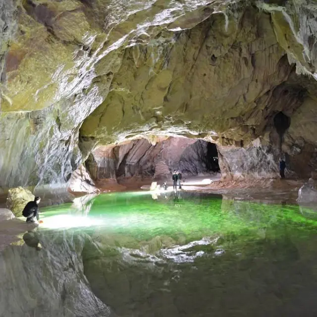 Explorateurs dans une grotte avec une lumière verte émanant d'un bassin