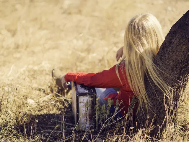 Blonde child sitting in a field with an animal