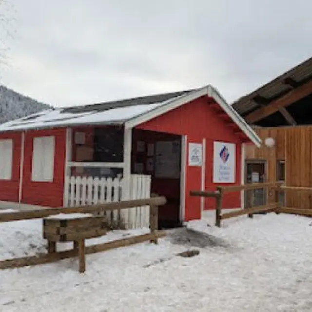 A small red cabin with a wooden fence in front, covered in snow