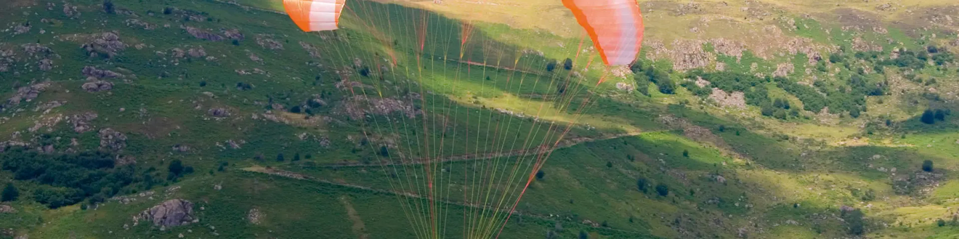 Person paragliding over green hills