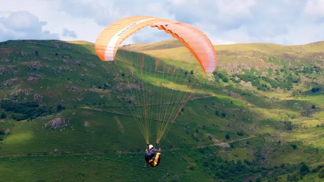 Person paragliding over green hills