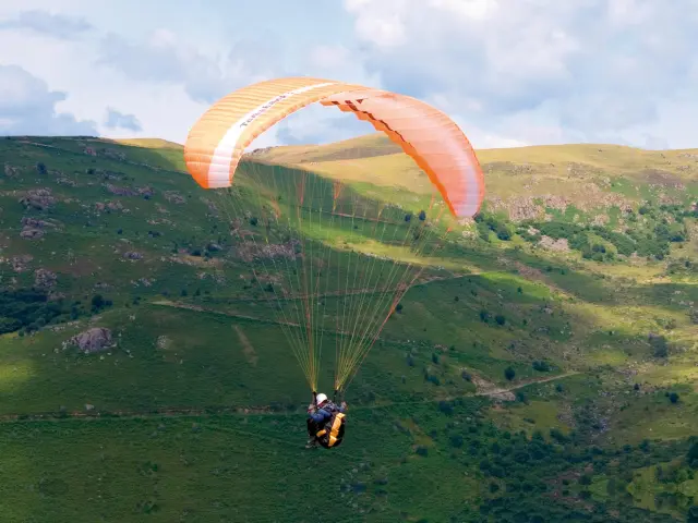 Person paragliding over green hills