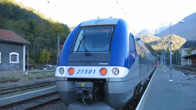 Blue and gray train at the station with mountains in the background