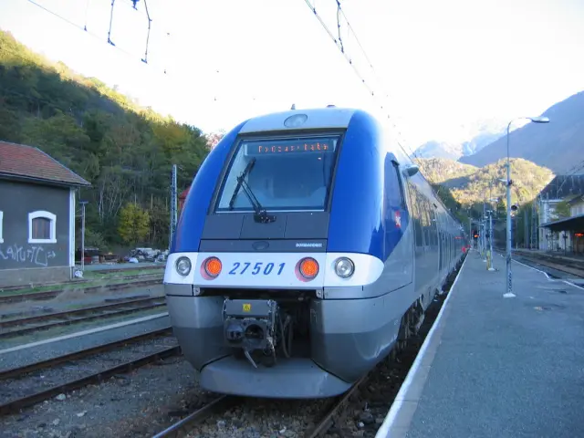 Blue and gray train at the station with mountains in the background
