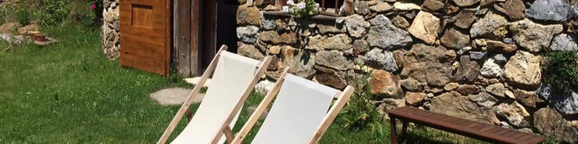 Stone cabin with two white deck chairs and a wooden bench