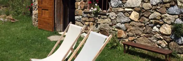 Stone cabin with two white deck chairs and a wooden bench