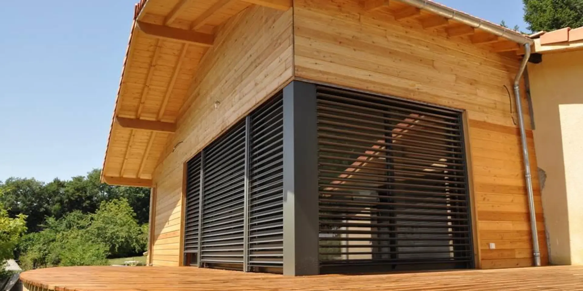 Maison en bois avec une grande terrasse en bois et des volets fermés