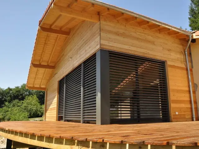 Maison en bois avec une grande terrasse en bois et des volets fermés