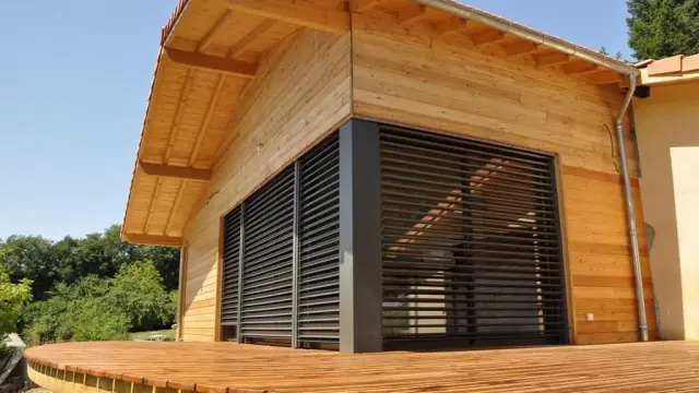 Maison en bois avec une grande terrasse en bois et des volets fermés